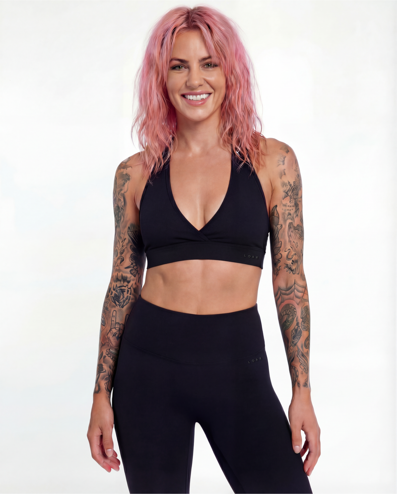 Front view of the LOAR black Halo Flex Halter and seamless leggings. Alternative athleisure from The Hero Collection, featuring a tattooed model in dark gym wear.